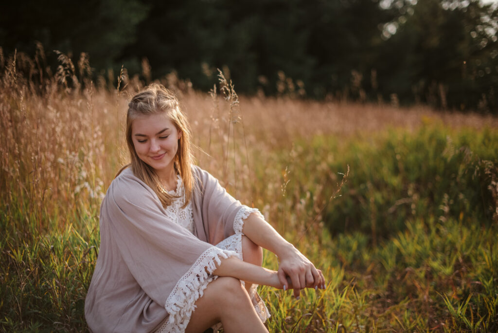 high school senior sitting in field during senior pictures in traverse city photographer