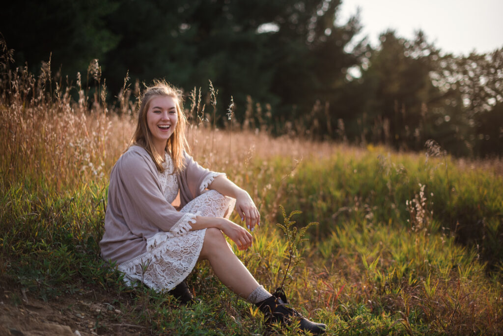 Grand Traverse Academy Senior sitting in tall grass during sunset during senior photos in traverse city