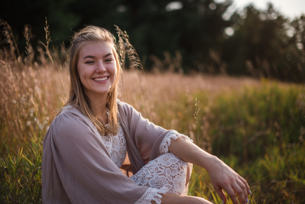 Grand Traverse Academy Senior sitting in tall grass during sunset during senior photography in traverse city