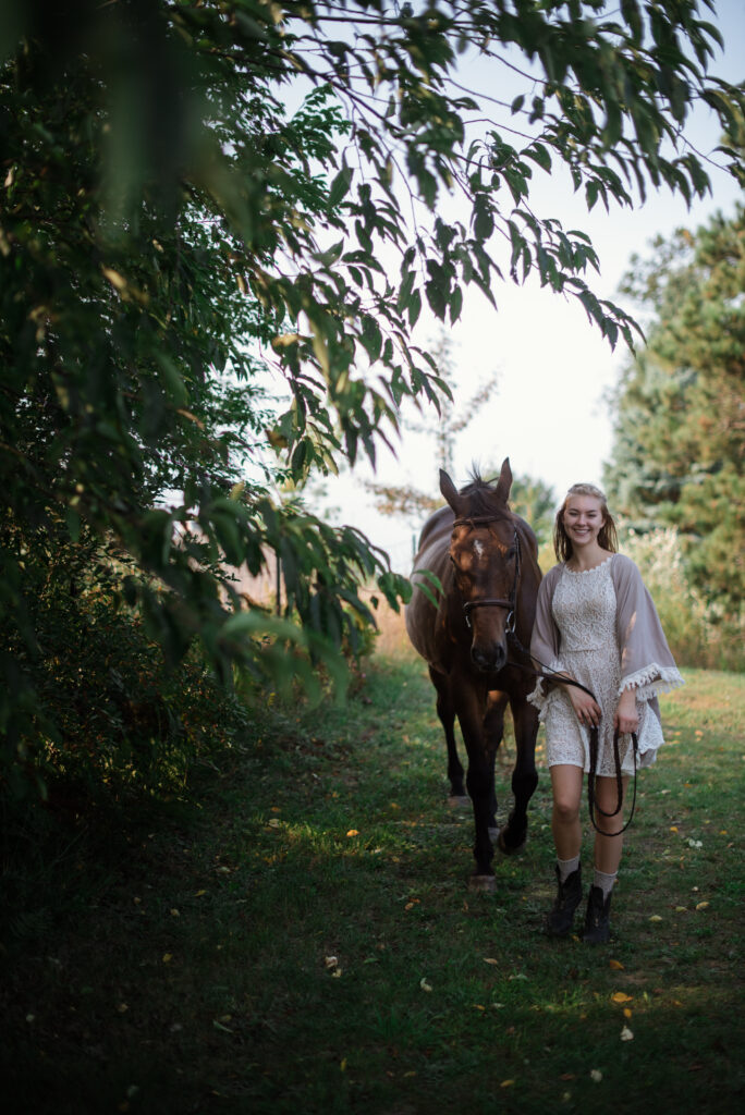 Grand Traverse Academy Senior standing under willow tree with horse during senior photos in traverse city