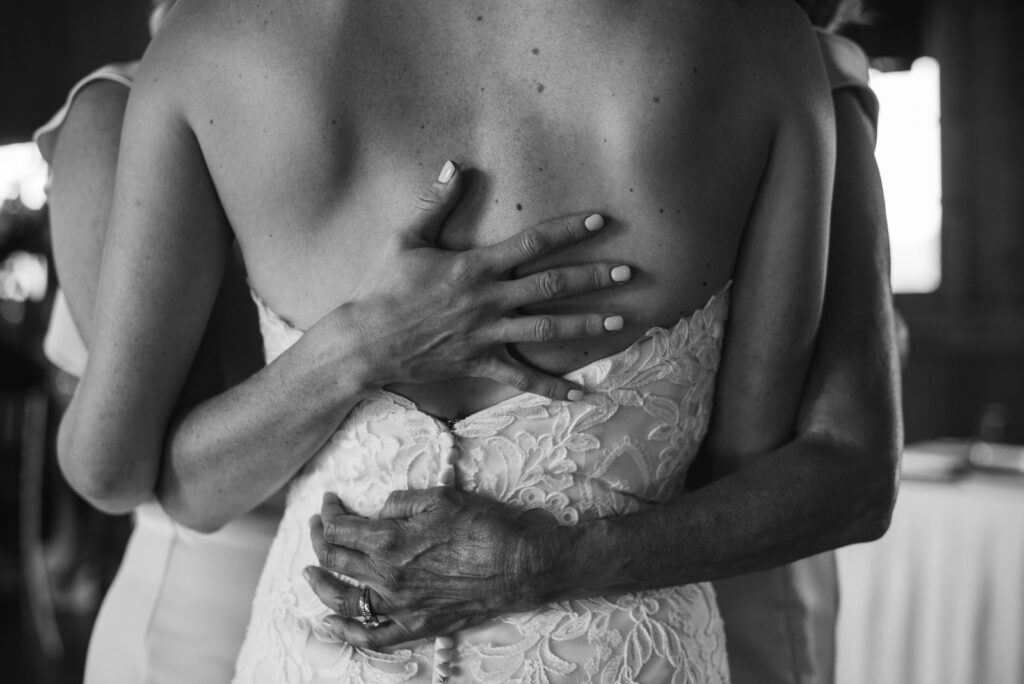 bride with sister and mothers hands on her back during mother daughter dance in traverse city michigan wedding