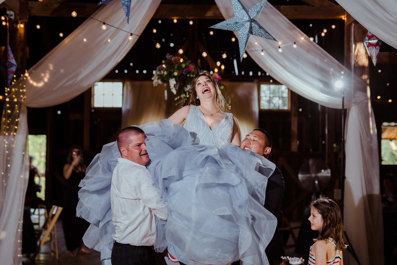 bride being lifted ona chair by wedding guests laughing candid reception in traverse city wedding