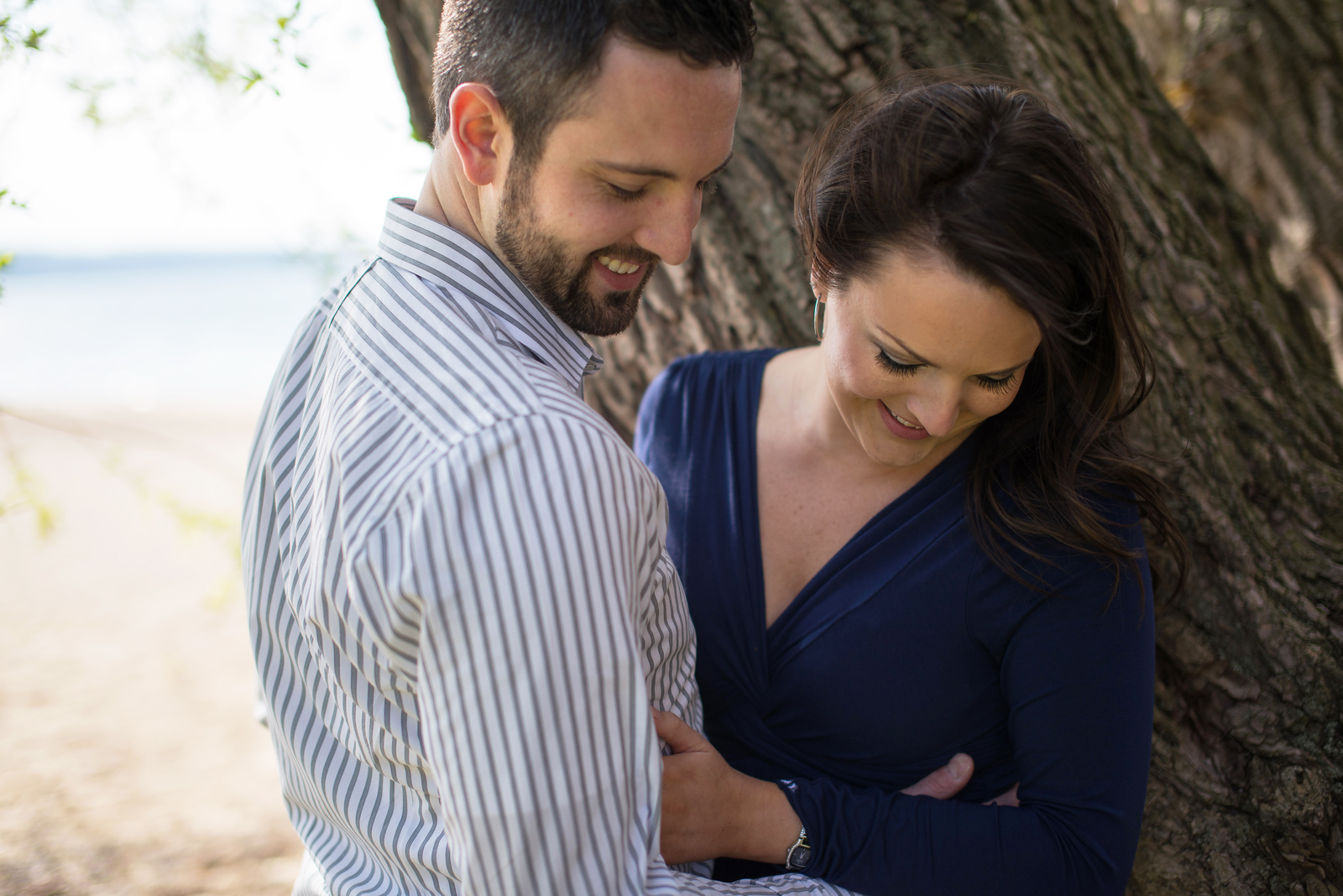 bride and groom candid engagement portrait cuddling under a tree next to grand traverse bay michigan