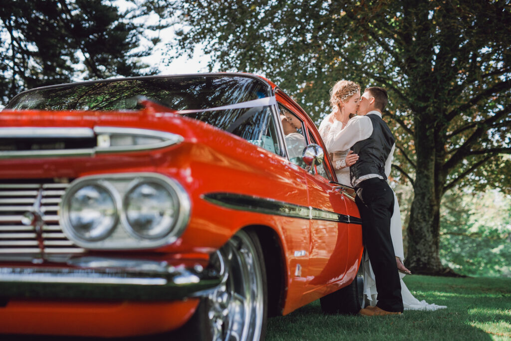 bride and groom kissing against classic car