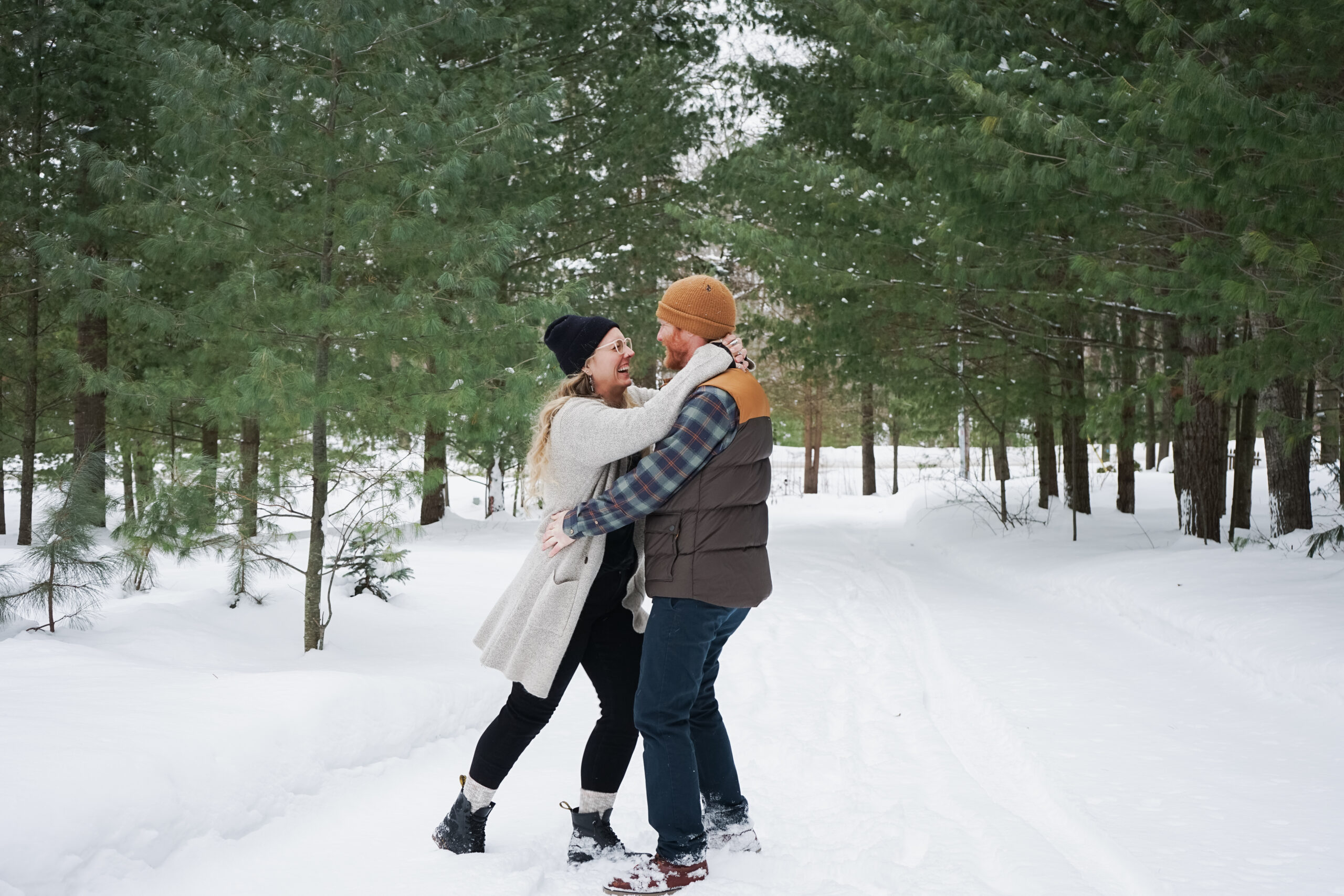 traverse city couple laughing during winter engagement photos in crystal lake michigan