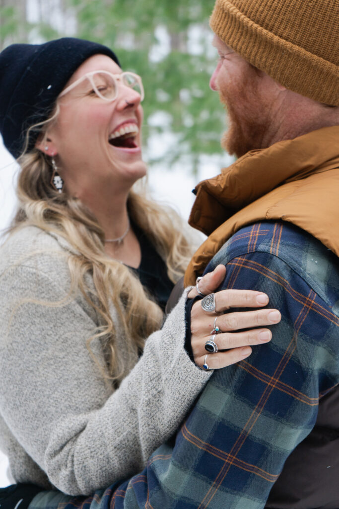traverse city couple laughing during winter engagement photos in crystal lake michigan