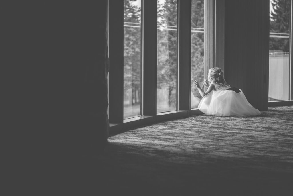 traverse city wedding venue with little girl in flower girl dress watching out the window