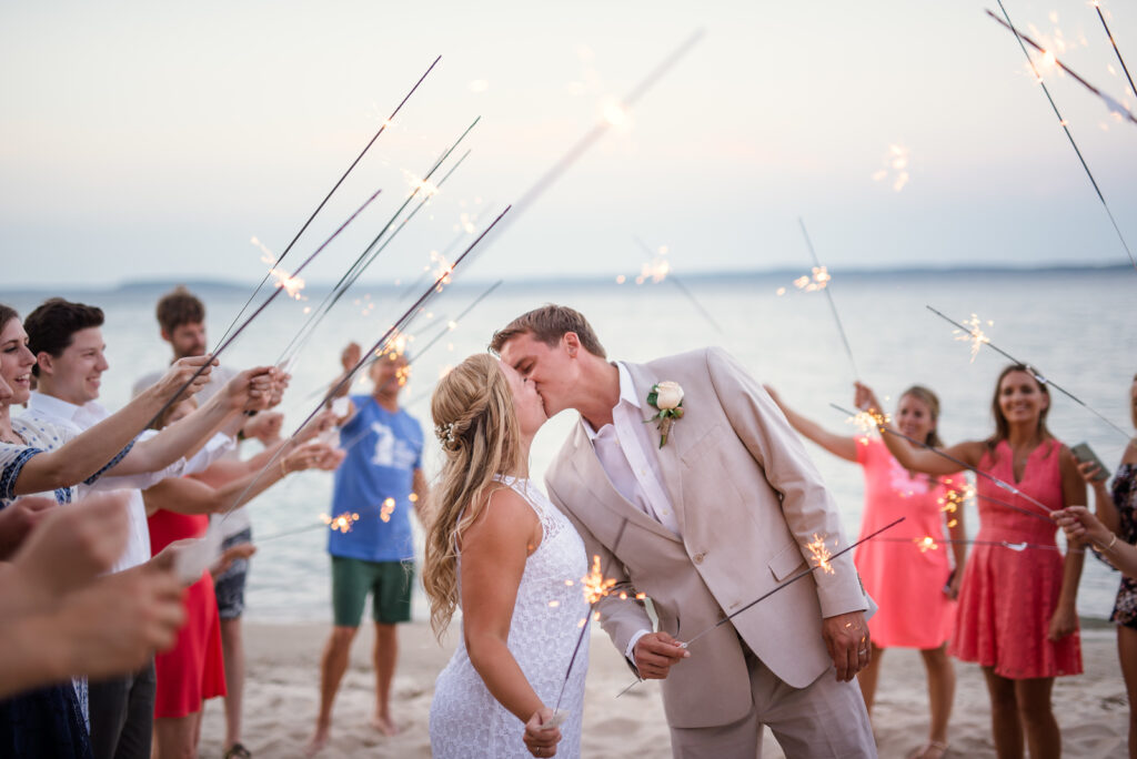 bride and groom standing on traverse bay beach under a tunnel of sparklers during wedding exit in traverse city michigan