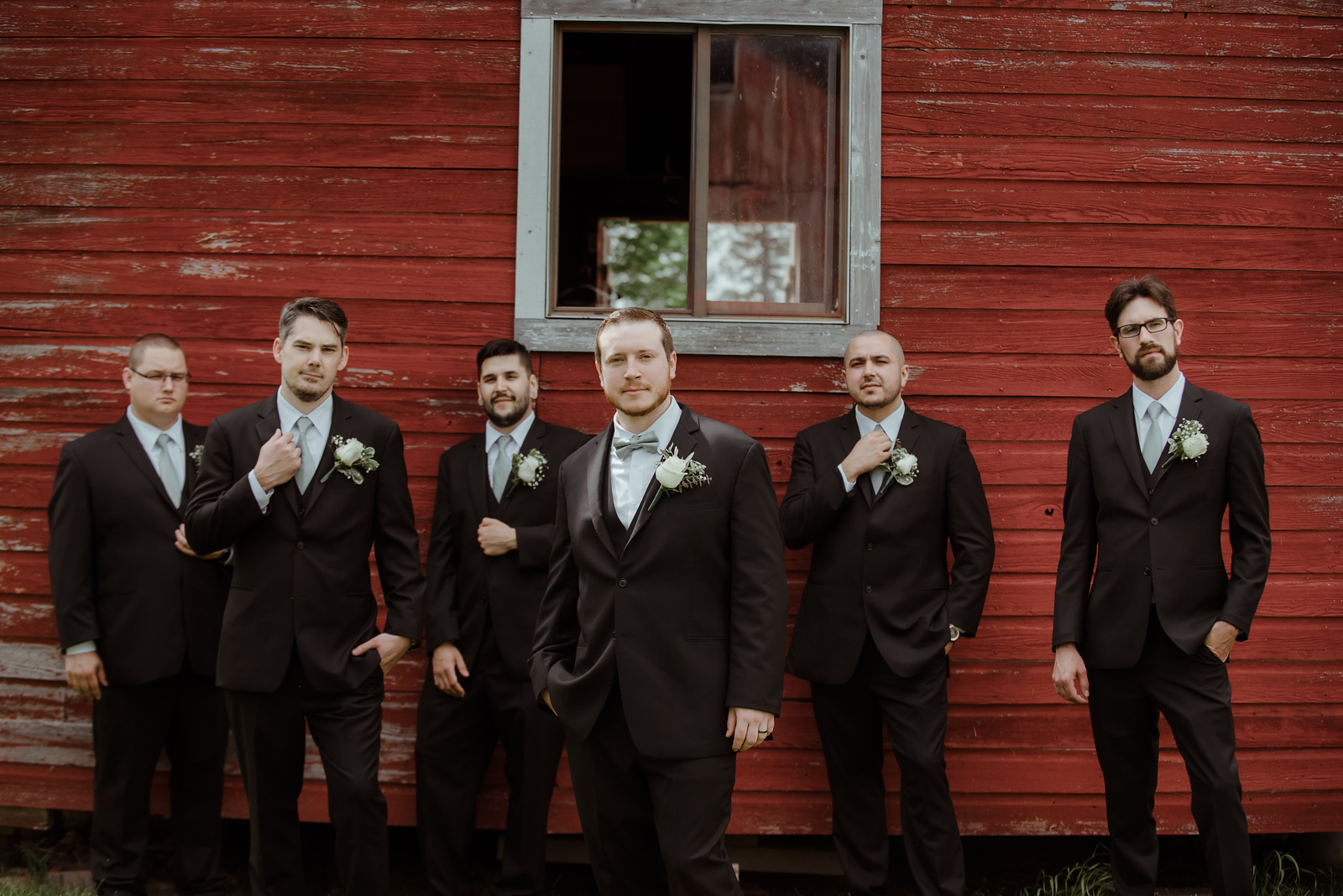 group of groomsmen standing against barn posing for wedding portraits in traverse city michigan
