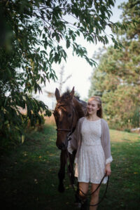 senior girl taking senior pictures walking in a field with her horse in traverse city michigan