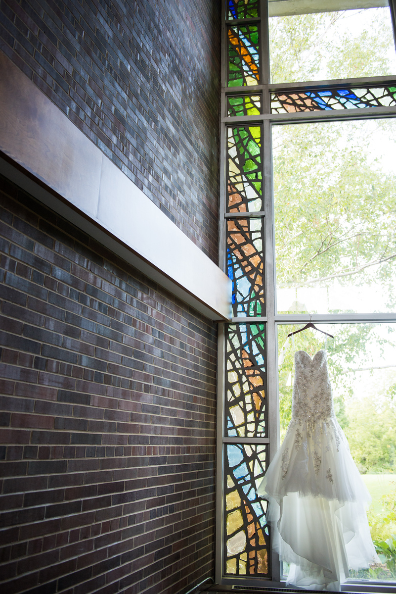 bridal gown hanging in cathedral stained glass window in traverse city church wedding