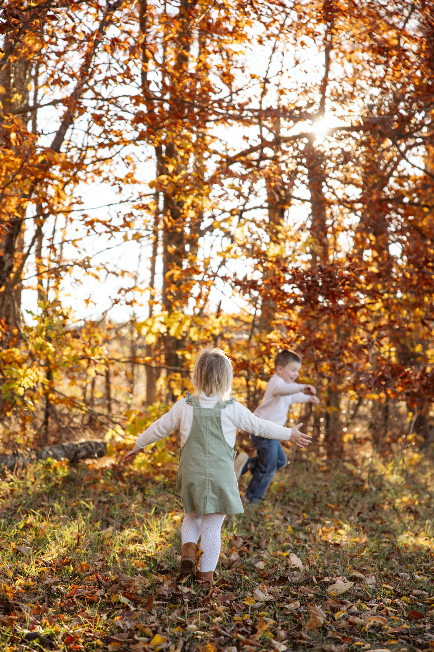 boy and girl running in leaves in a fall field during family pictures in empire michigan. Photo taken by traverse city photographer