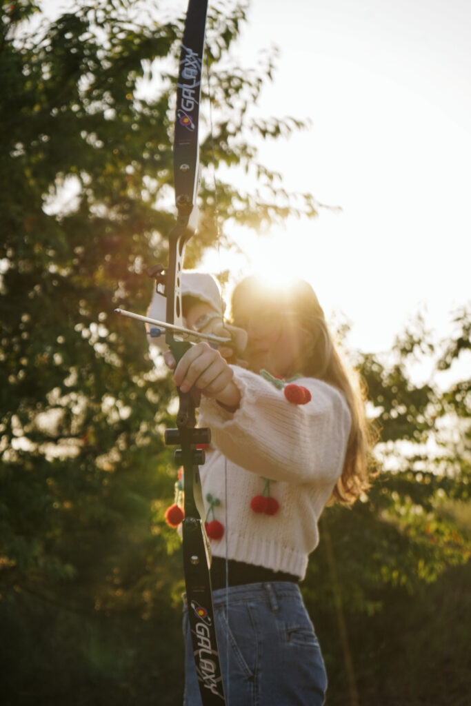 Girl standing in a field with a bow at golden hour during Senior photos. Photo by Traverse city photographer, Lina LaVonne Photography