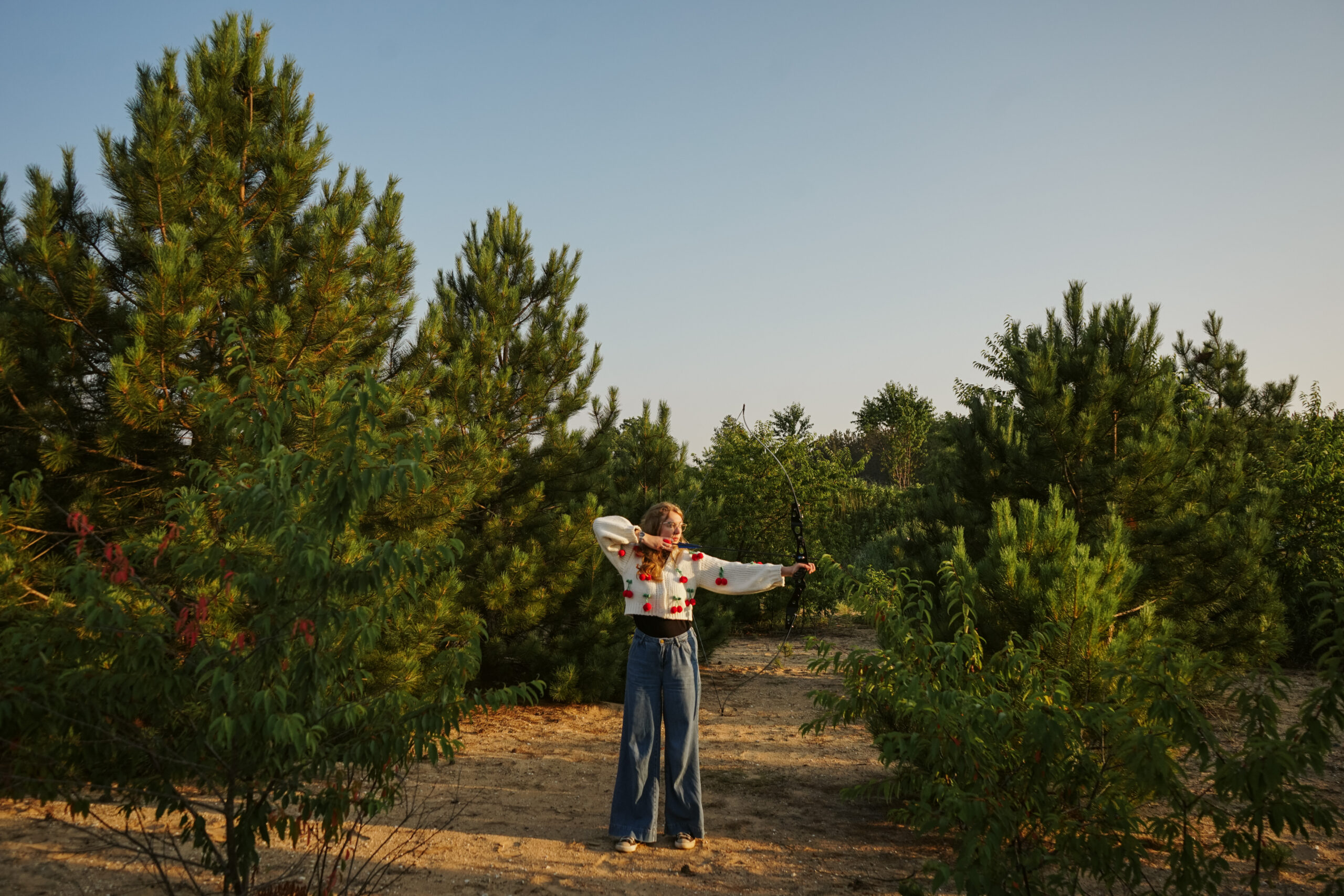 Girl standing in a field with a bow at golden hour during Senior photos. Photo by Traverse city photographer, Lina LaVonne Photography