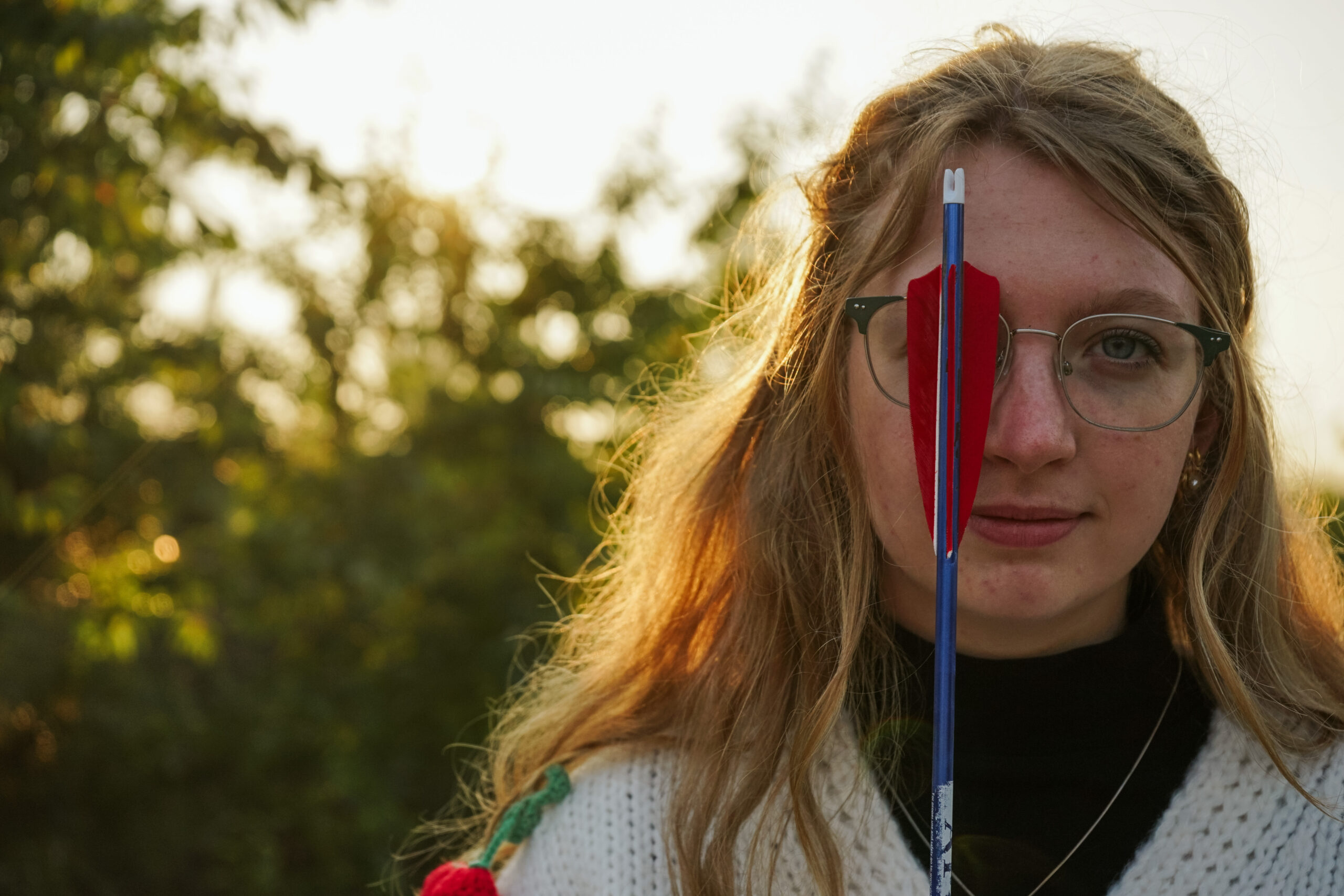Girl standing in a field with a bow at golden hour during Senior photos. Photo by Traverse city photographer, Lina LaVonne Photography