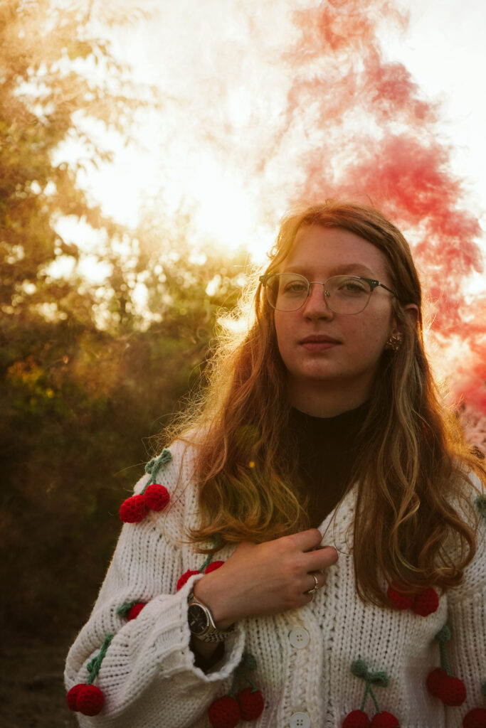 Girl standing in a field at golden hour with smoke bomb during Senior photos. Photo by Traverse city photographer, Lina LaVonne Photography