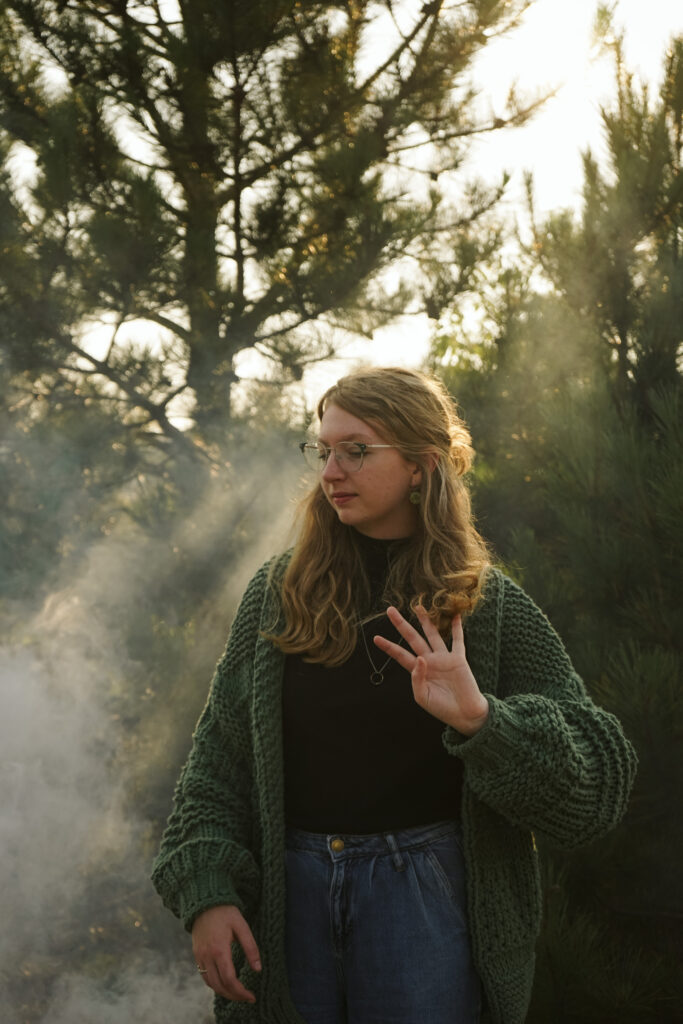 Girl standing in a field with a smoke bomb at golden hour during Senior photos. Photo by Traverse city photographer, Lina LaVonne Photography