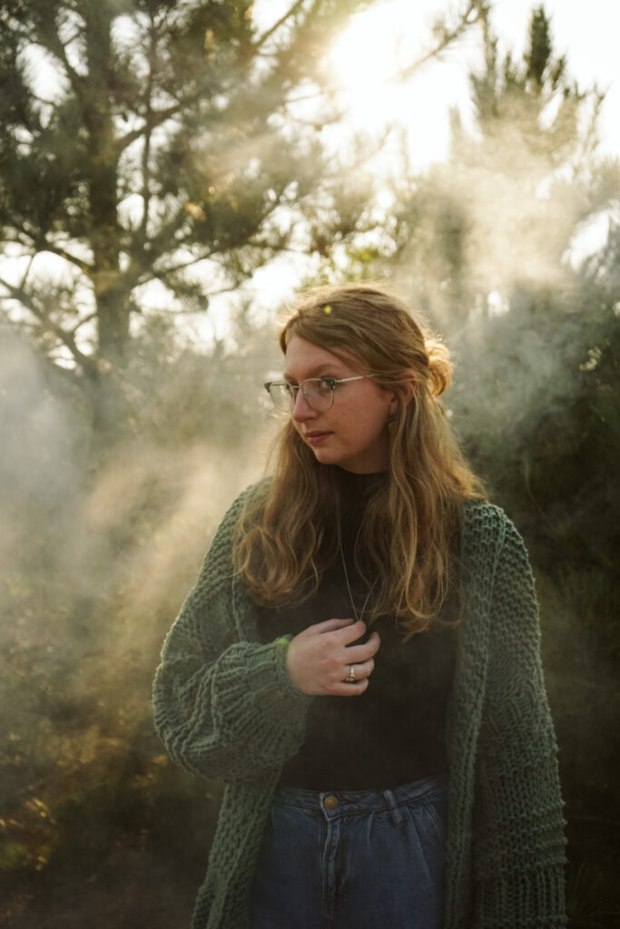 Girl standing in a field with a smoke bomb at golden hour during Senior photos. Photo by Traverse city photographer, Lina LaVonne Photography