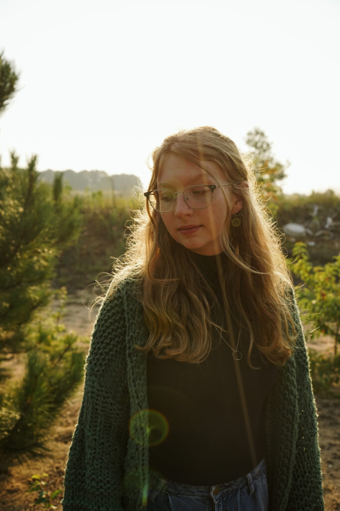 Girl standing in a field with a smoke bomb at golden hour during Senior photos. Photo by Traverse city photographer, Lina LaVonne Photography