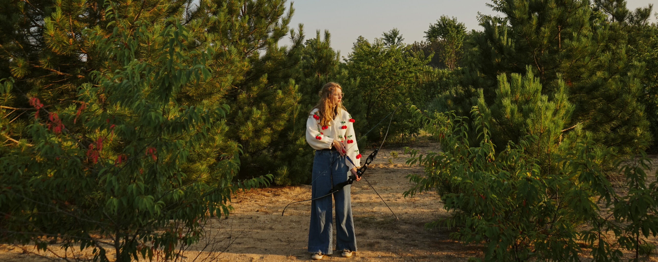 high school senior standing in field with bow and arrow during engagement photos in traverse city