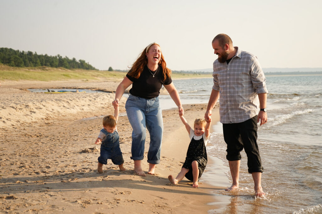 family holding hands on a beach laughing in empire michigan
