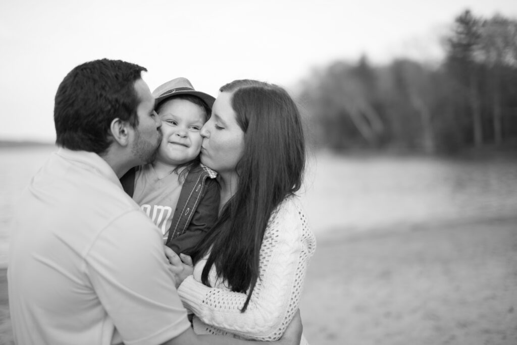 mother and father kissing their son on long lake beach in traverse city