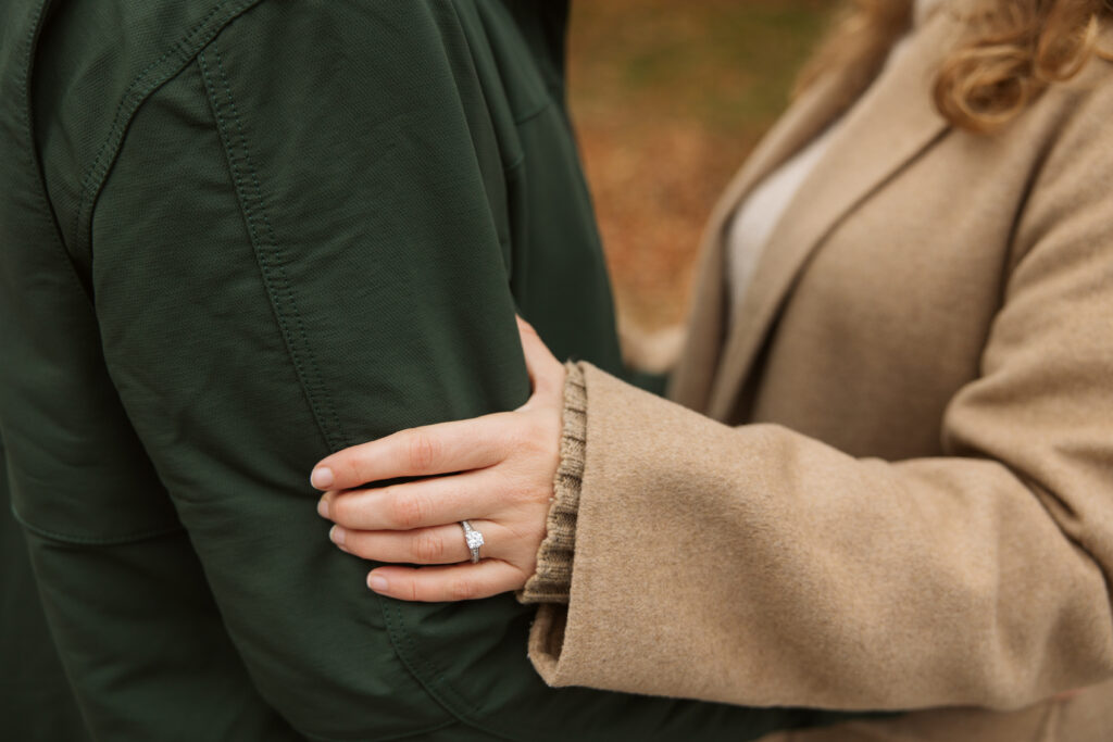 close up of engagement ring on brides hand resting on grooms arm during fall engagement photos on empire beach in michigan. Photo by Traverse city wedding photographer lina lavonne photography