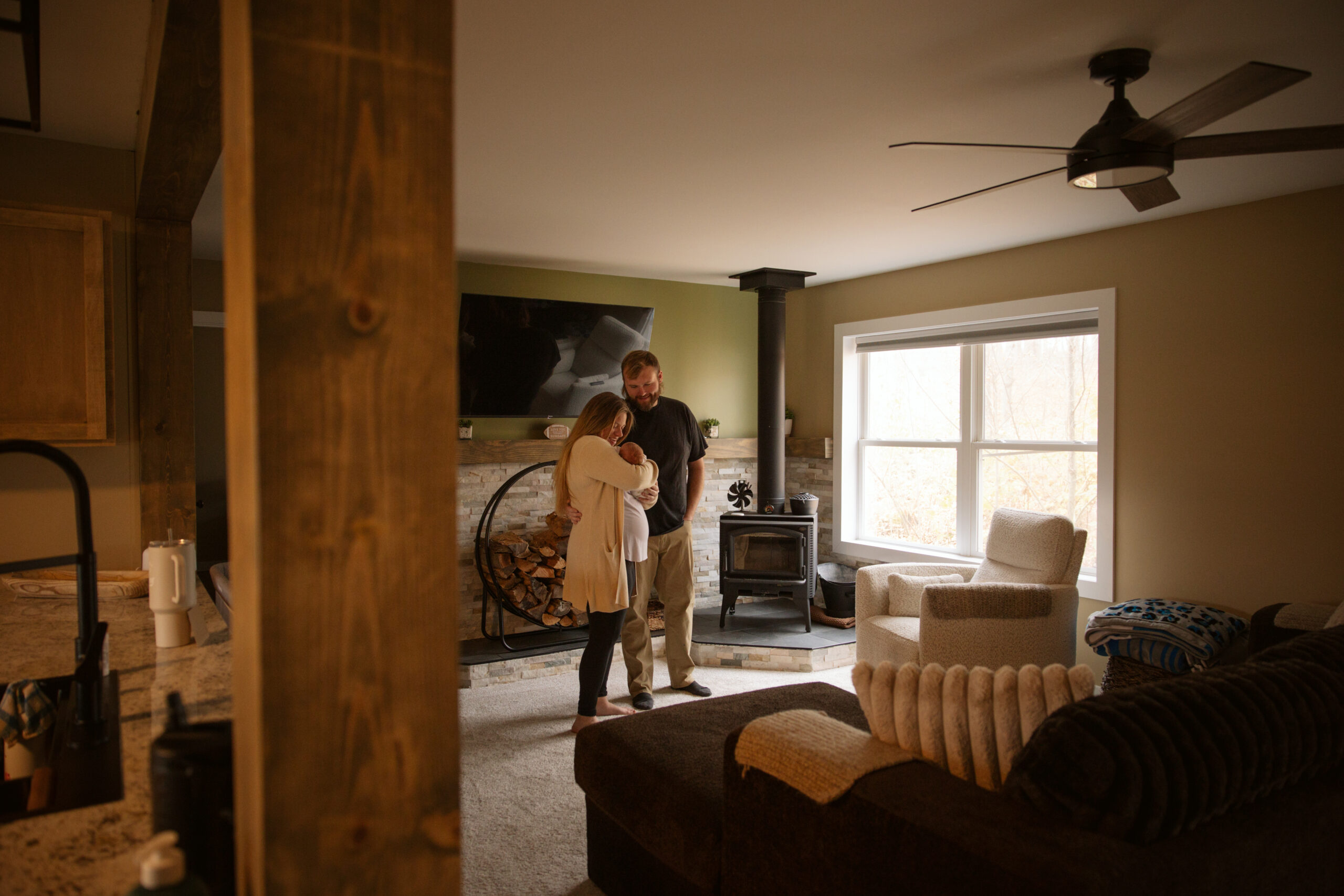 husband and wife holding newborn baby in their home during newborn photos in traverse city michigan