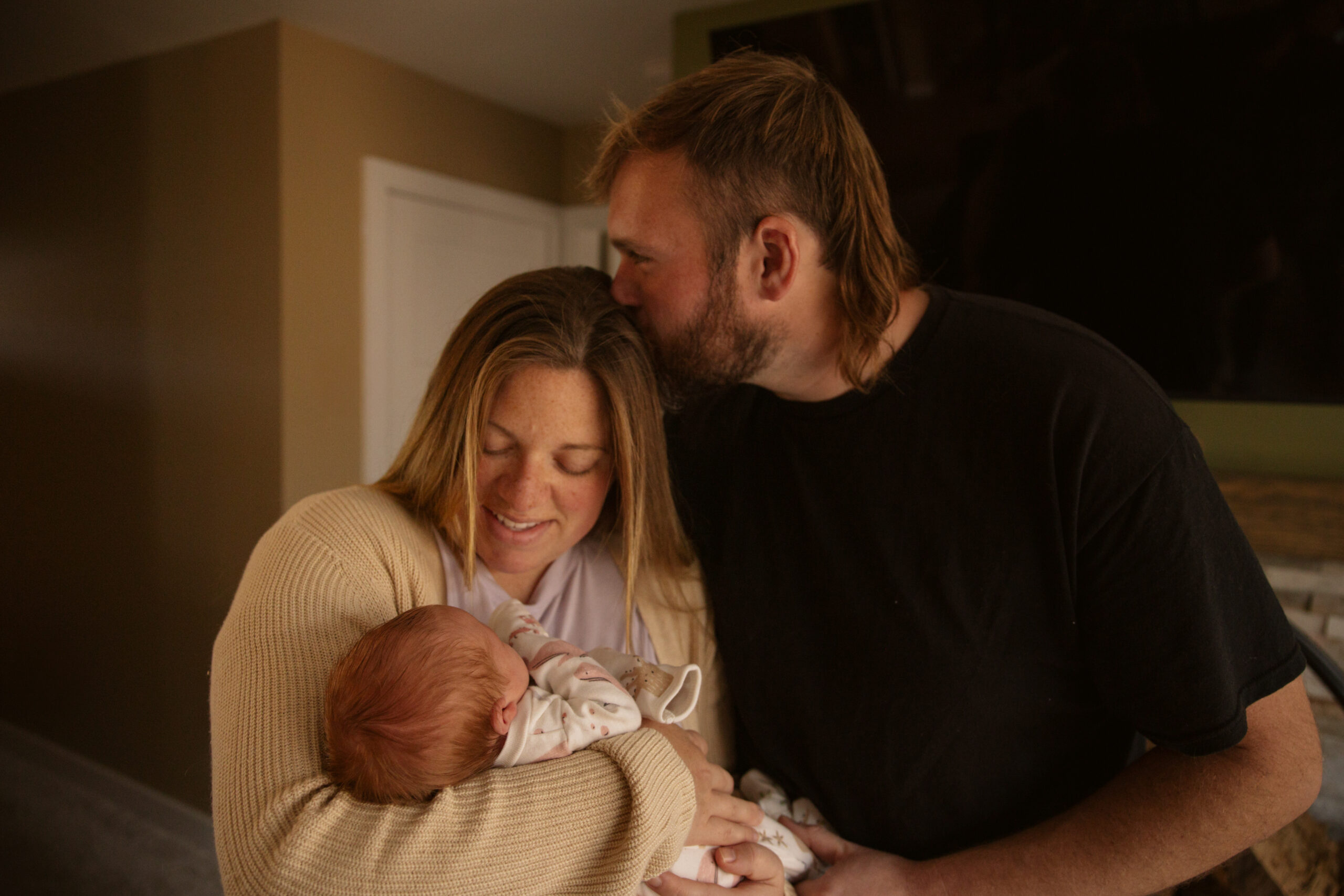 husband kissing his wifes head while she holds their newborn baby during family photos in traverse city michigan