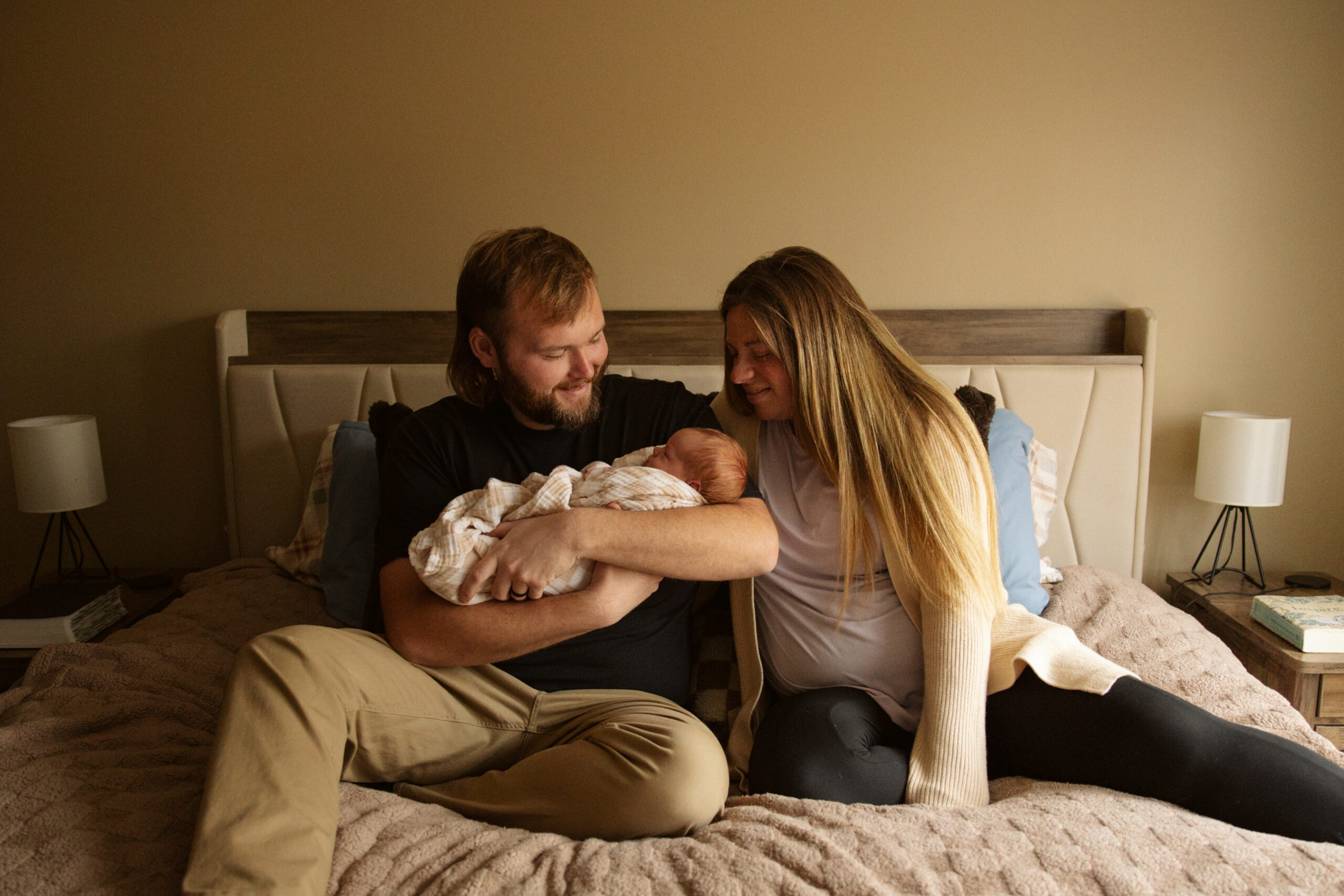 mother and father sitting on a bed holding their baby during newborn photos in traverse city michigan