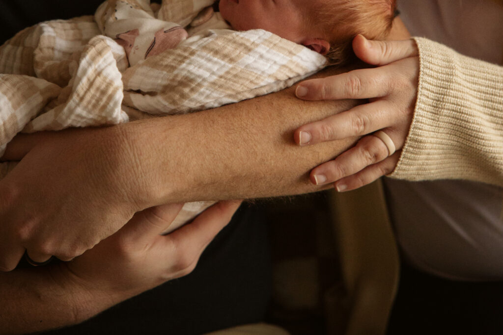 close up of the hands of a mother and father holding a baby during newborn photos in traverse city michigan