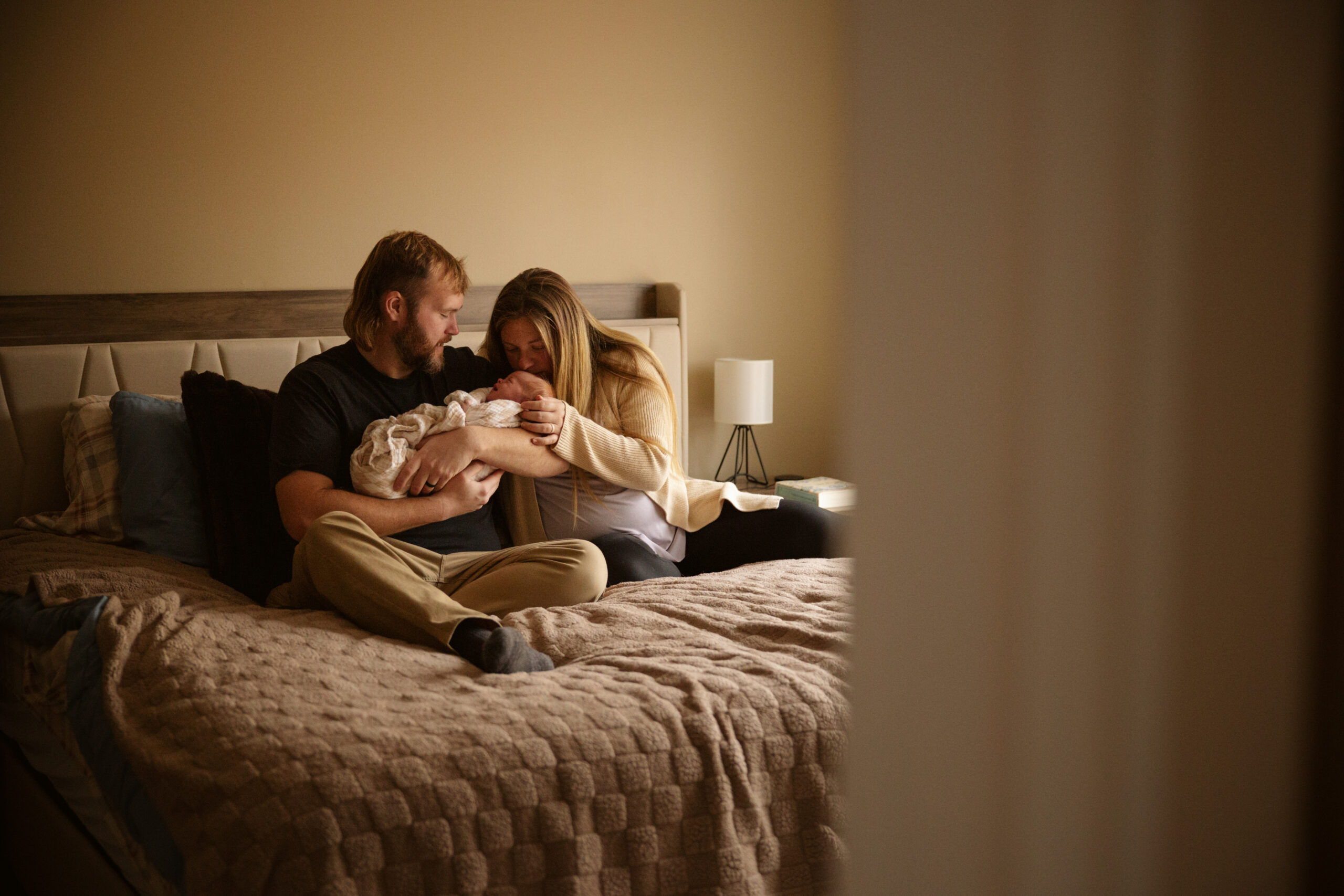 mother and father sitting on a bed holding a newborn