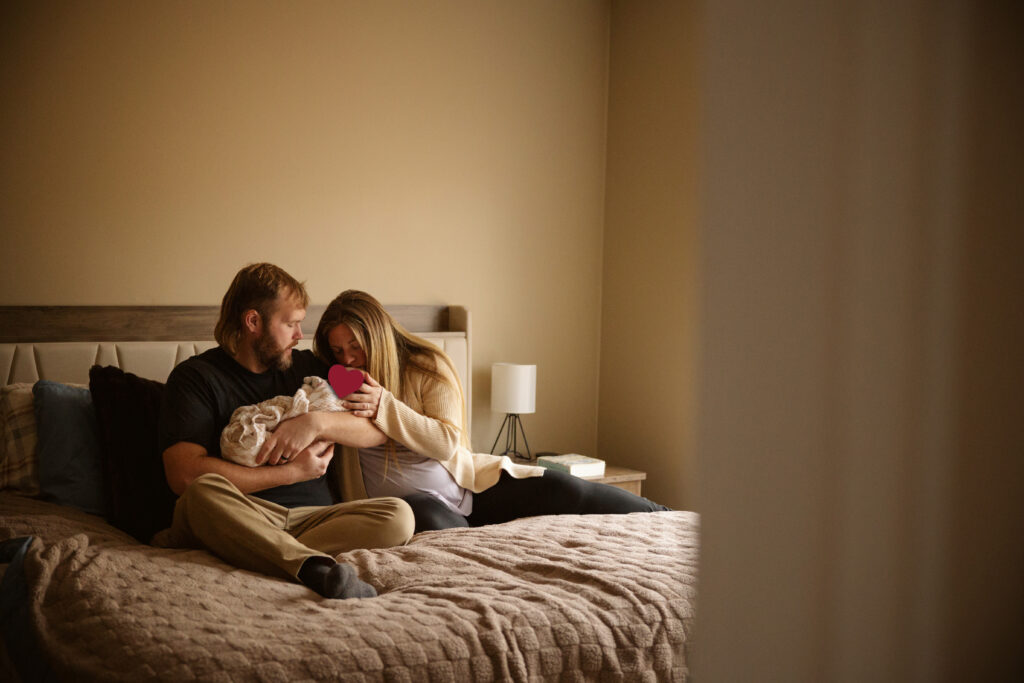 husband and wife sitting on bed holding their newborn baby during family photos in traverse city michigan