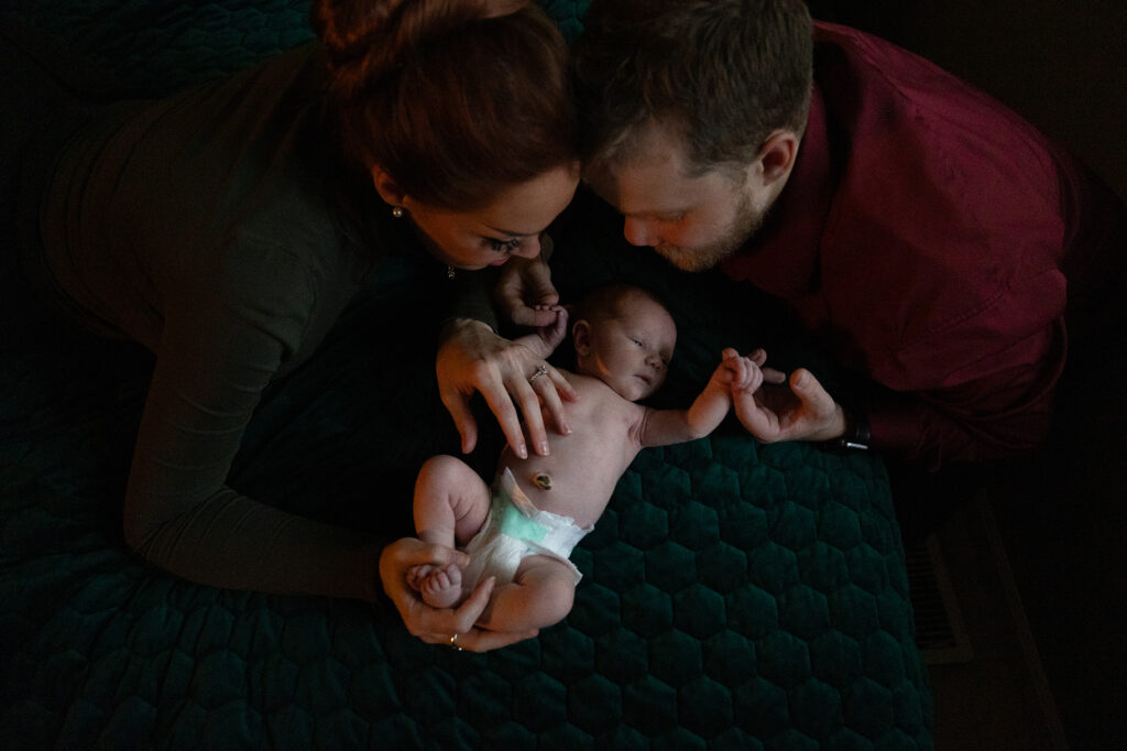 top view of mother and father holding a baby on their bed during newborn photos in traverse city. Photo by Traverse City Photographer Lina Lavonne Photography