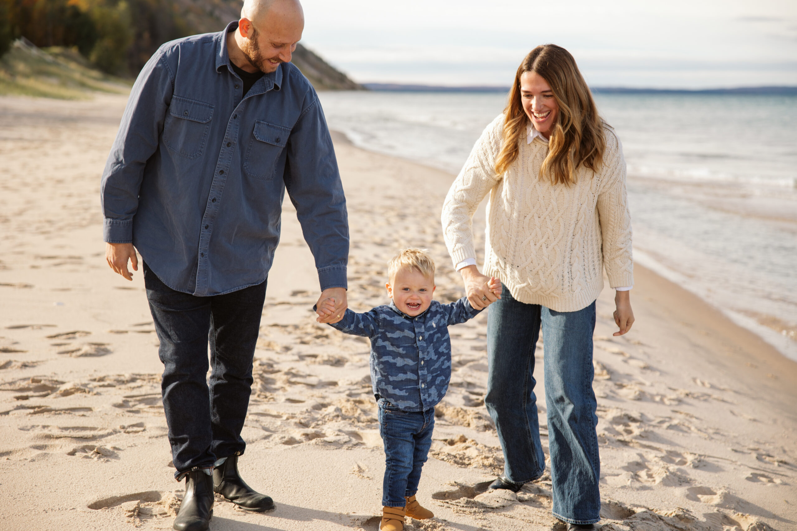 mom and dad swinging little boy on empire beach during fall family portraits in Empire. Photo by Lina Lavonne photography a traverse city photographer