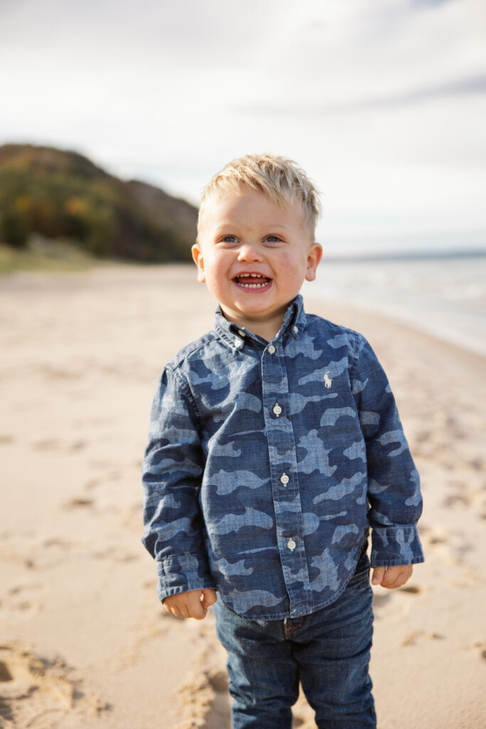 Little boy smiling on beach during family fall photos. Photo by Lina Lavonne photography a traverse city photographer