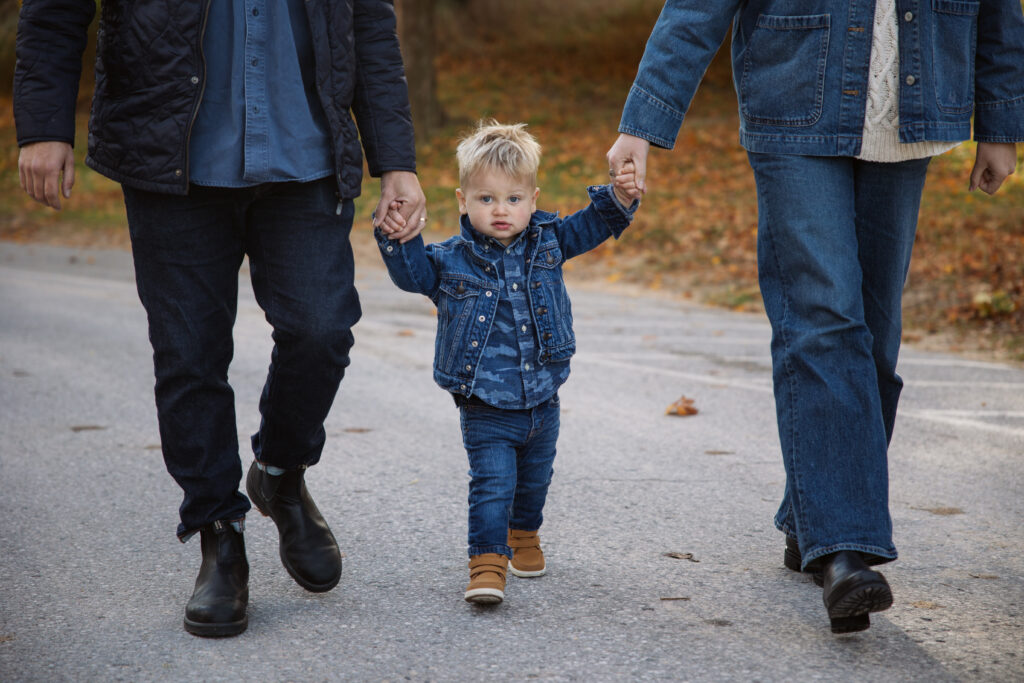 family of three walking down a fall road in northern michigan holding hands during family portraits in Empire. Photo by Lina Lavonne photography a traverse city photographer