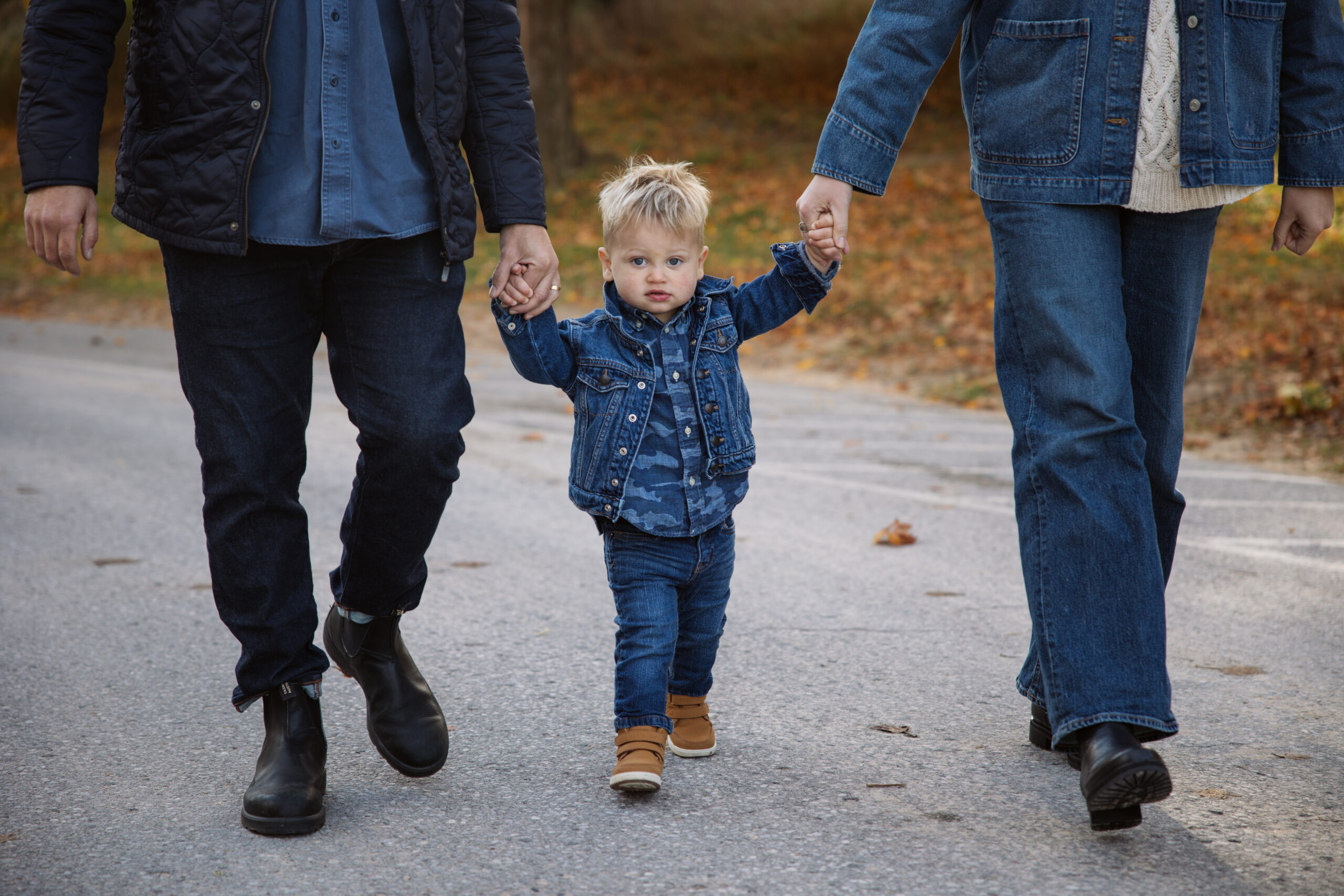 family of three walking down a fall road in northern michigan holding hands during family portraits in Empire. Photo by Lina Lavonne photography a traverse city photographer