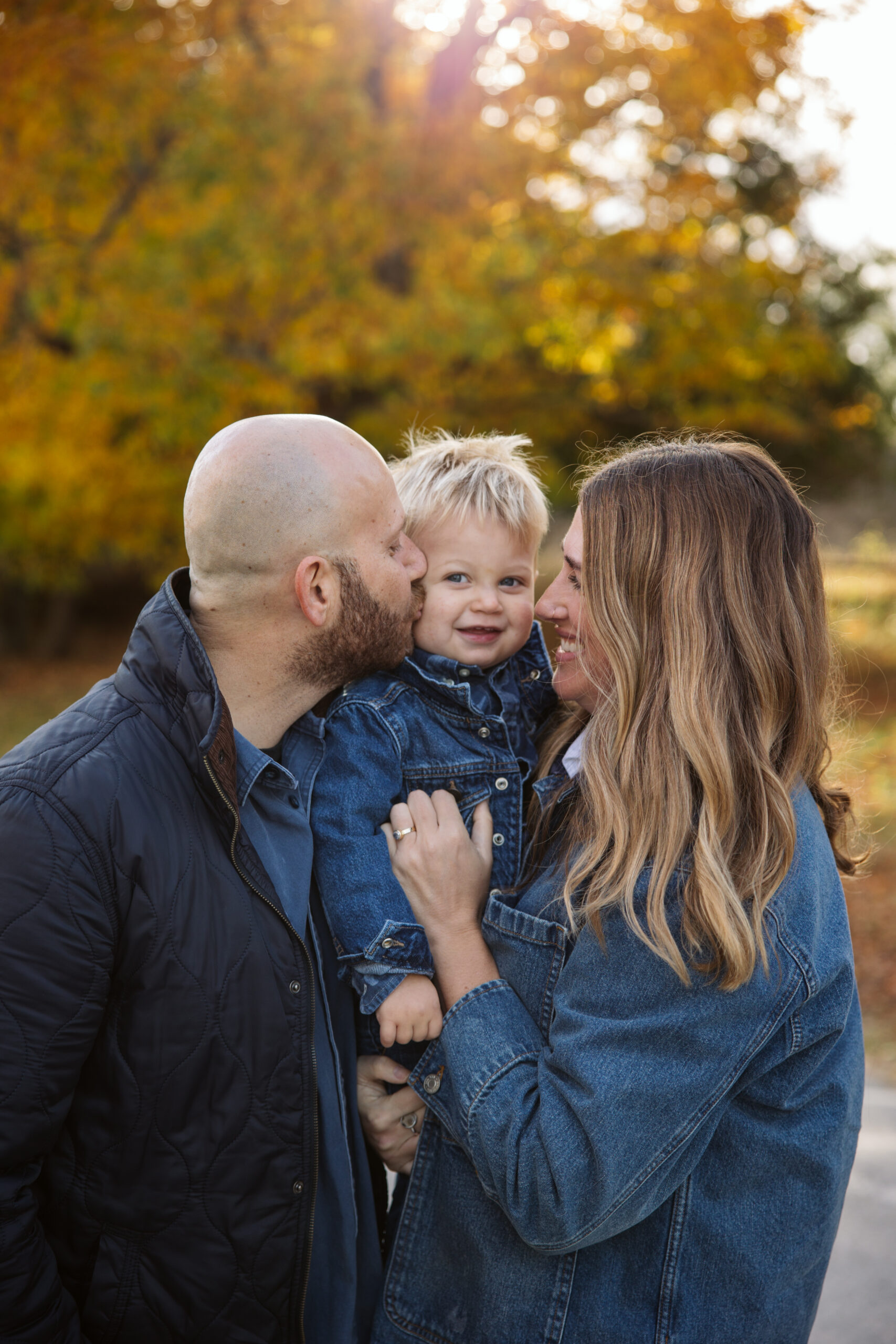 family of three kissing little boy during fall family portraits in Empire. Photo by Lina Lavonne photography a traverse city photographer