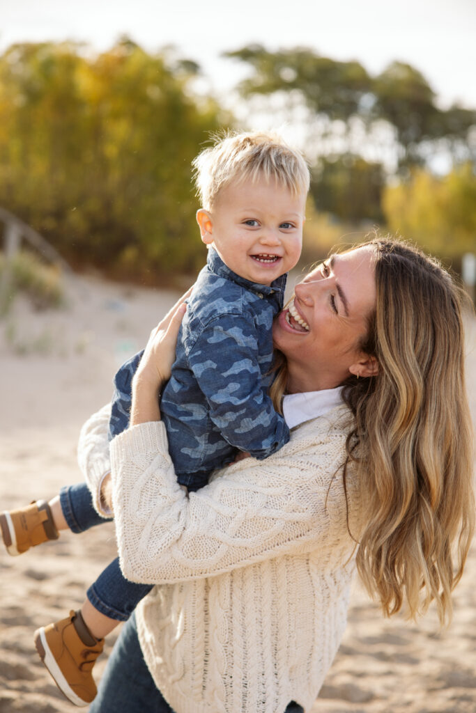mom spinning little boy in her arms backlit during fall family portraits in Empire. Photo by Lina Lavonne photography a traverse city photographer