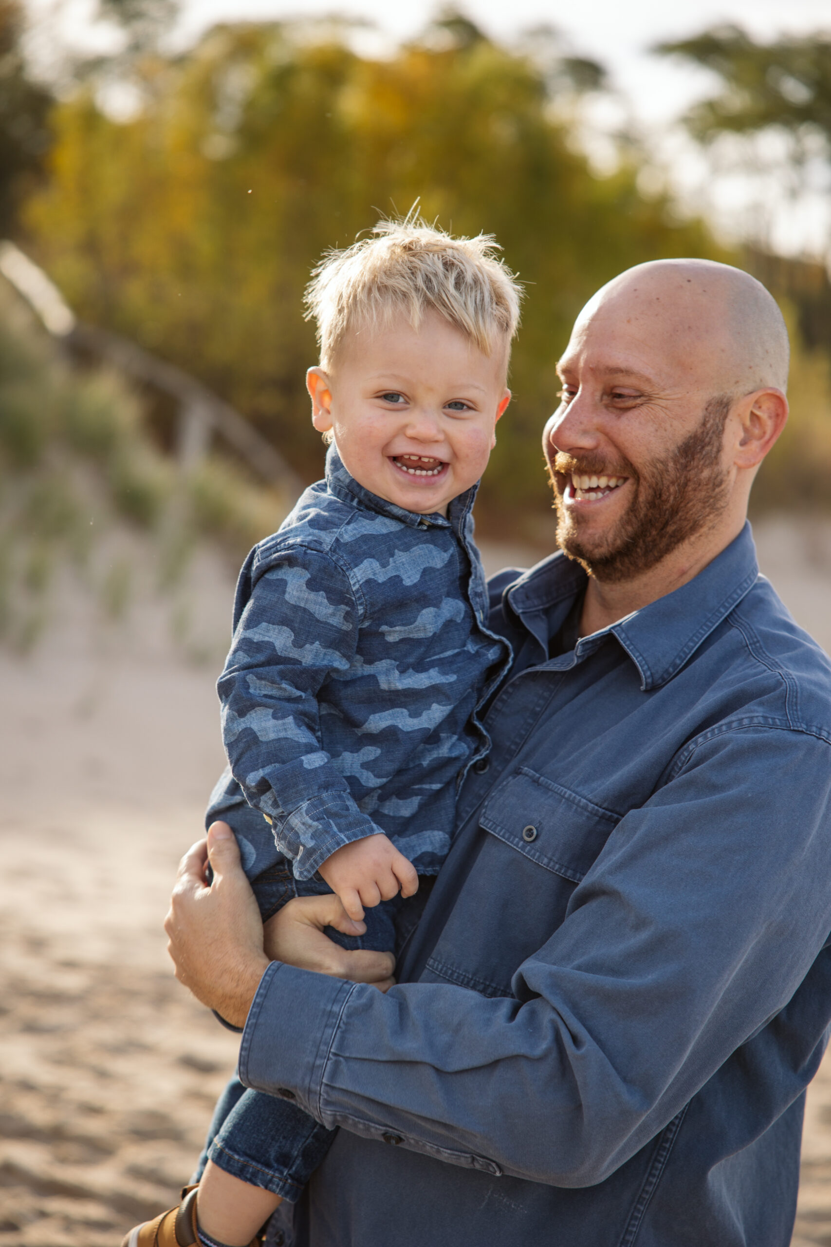 dad holding son on beach during fall family portraits in Empire. Photo by Lina Lavonne photography a traverse city photographer