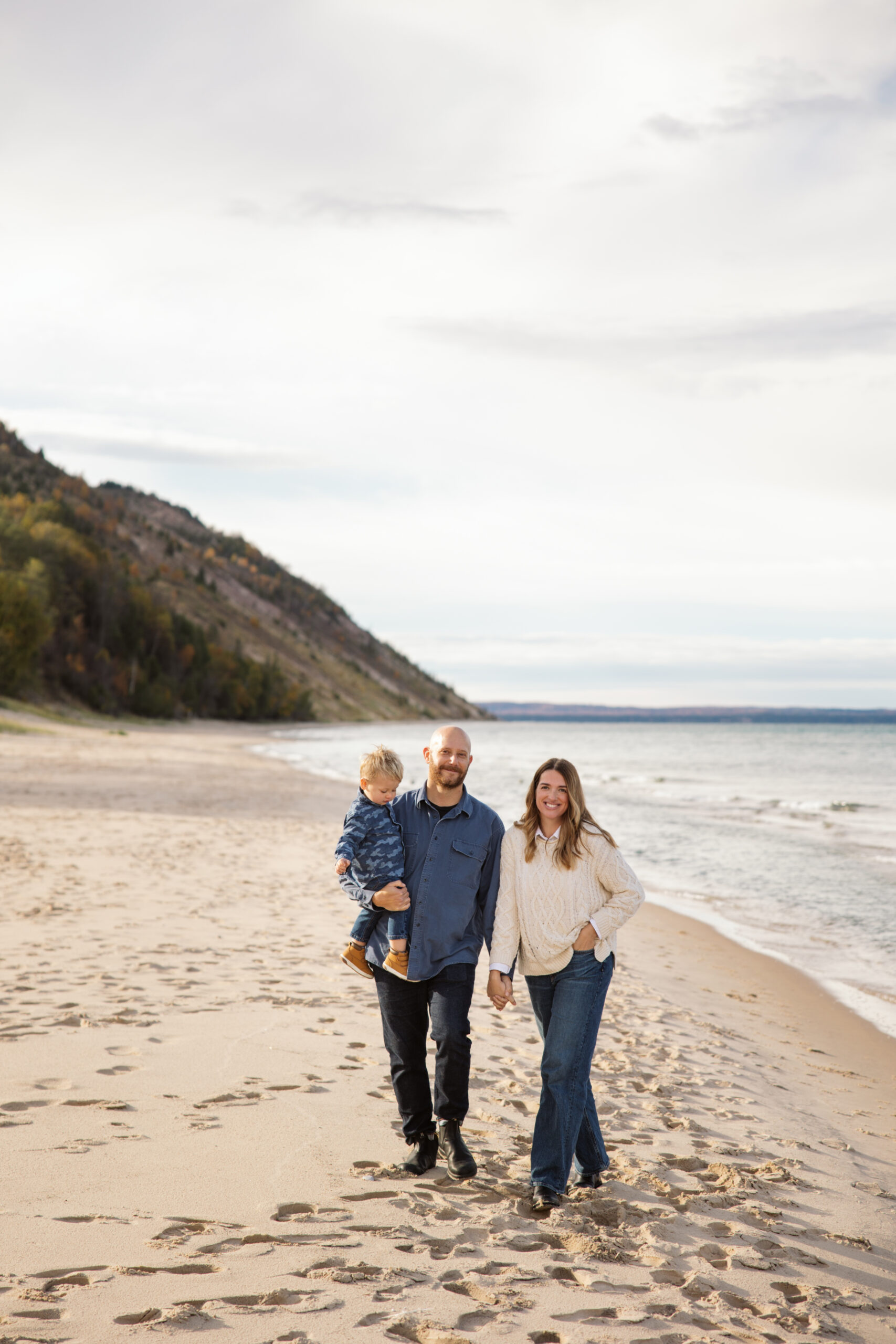 mom dad and little boy walking on empire beach during fall family portraits in Empire. Photo by Lina Lavonne photography a traverse city photographer