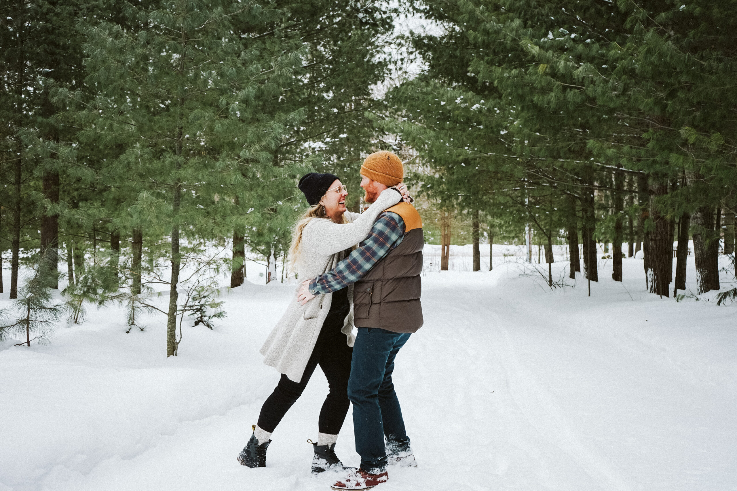 bride and groom dancing in the snow in northern michigan woods during engagement photos. Photo taken by Traverse city photographer Lina Lavonne Photography