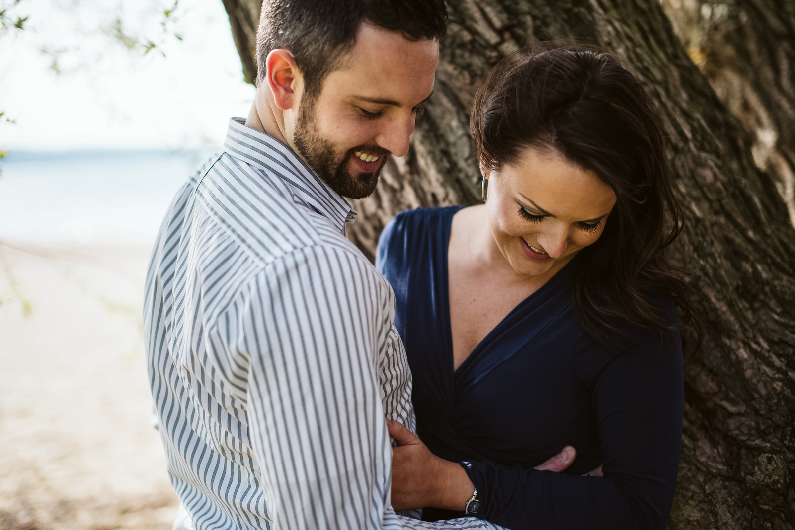 engaged couple hugging against tree on Traverse City beach on Old Mission Peninsula during engagement photos. Photo by Traverse City Photographer, Lina Lavonne Photography