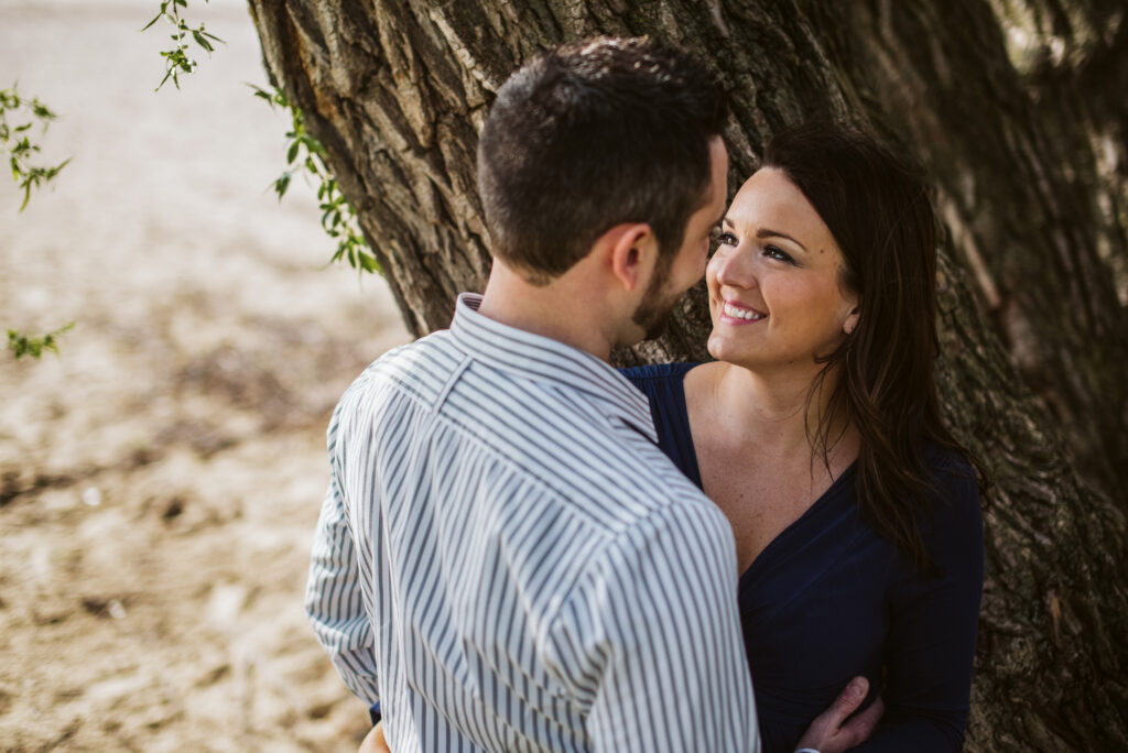 engaged couple hugging against tree on Traverse City beach on Old Mission Peninsula during engagement photos. Photo by Traverse City Photographer, Lina Lavonne Photography