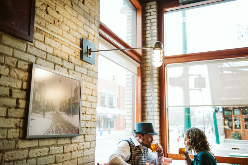 Couple sitting in bar downtown traverse city drinking beer during engagement photos by local wedding photographer Lina LaVonne Photography.