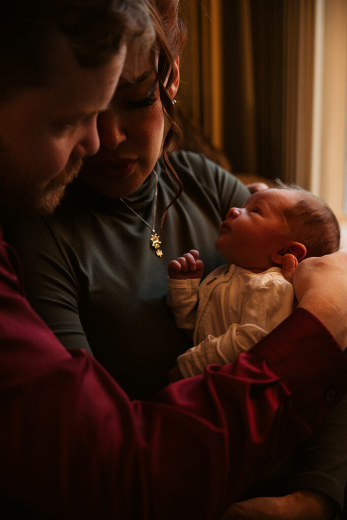 baby in the hands of his mother and father during in home newborn photos in traverse city. Photo by Traverse City Photographer Lina Lavonne Photography