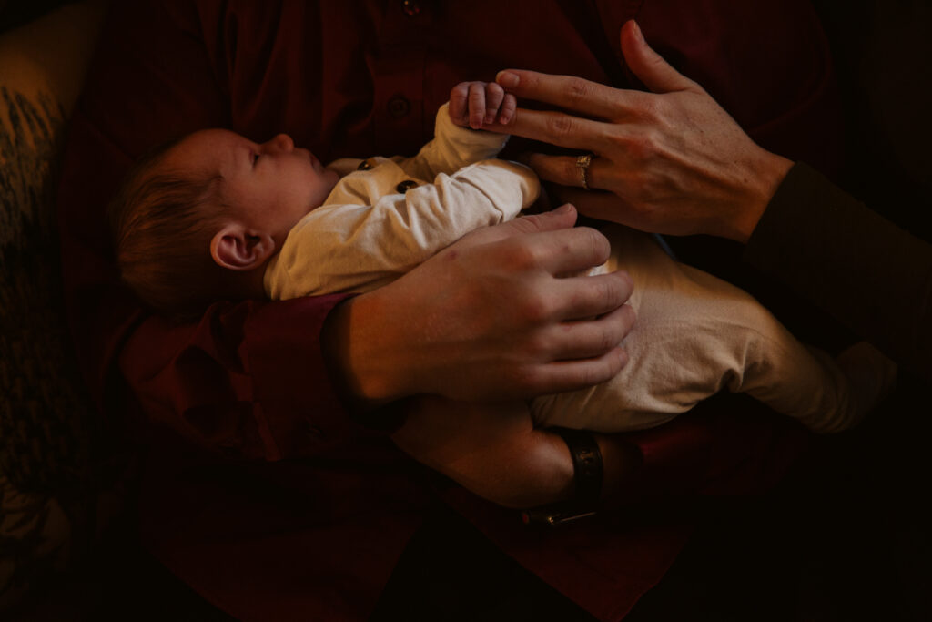 baby in the hands of his mother and father during in home newborn photos in traverse city. Photo by Traverse City Photographer Lina Lavonne Photography