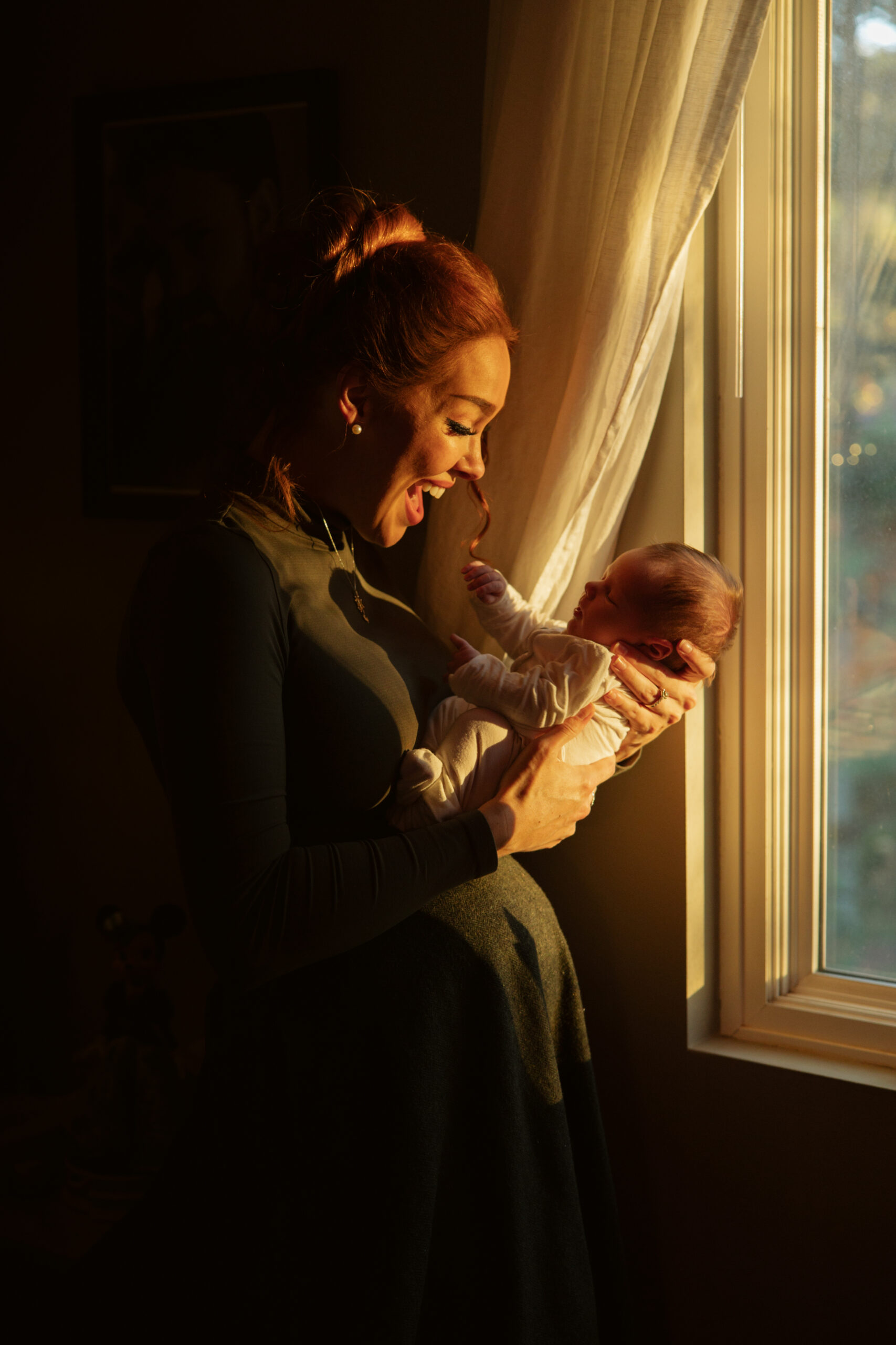 mom and baby standing in sunset light in their home window during newborn photos in traverse city. Photo by Traverse City Photographer Lina Lavonne Photography
