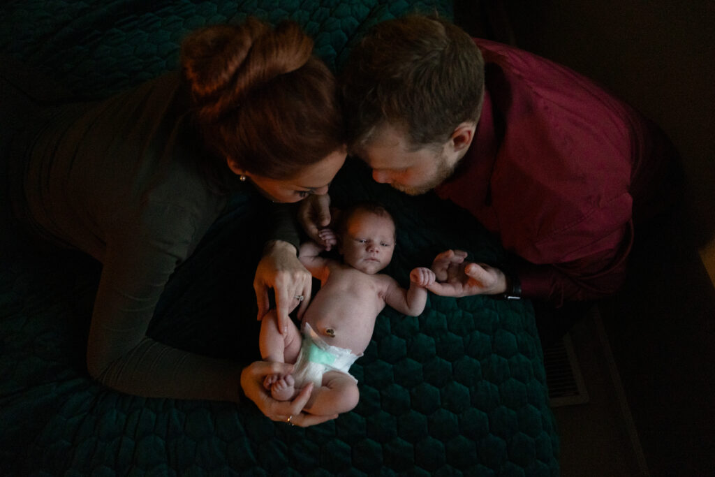 top view of mother and father holding a baby on their bed during newborn photos in traverse city. Photo by Traverse City Photographer Lina Lavonne Photography